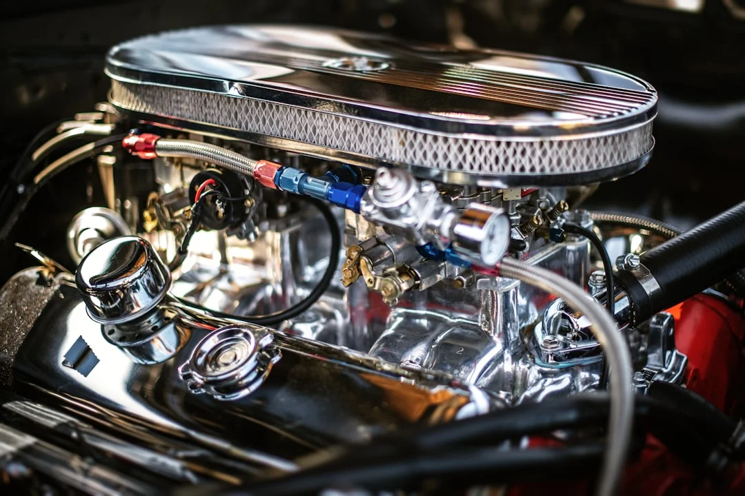 A classic muscle car engine bay mid-EFI conversion, throttle body mounted on a freshly painted intake manifold, AN fuel lines routed cleanly, wideband O2 sensor wiring visible, shop lighting overhead